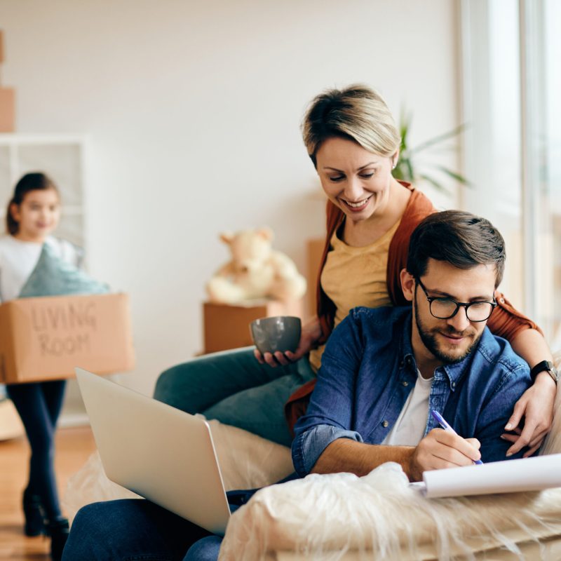 Happy man using laptop and going through paperwork while moving into a new home with his wife and daughter.